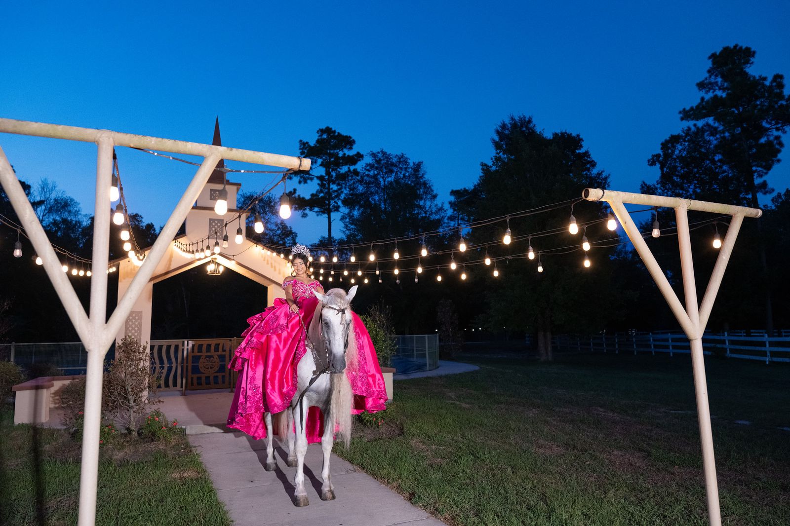 Quinceañera on horseback under string lights at dusk by the outdoor chapel