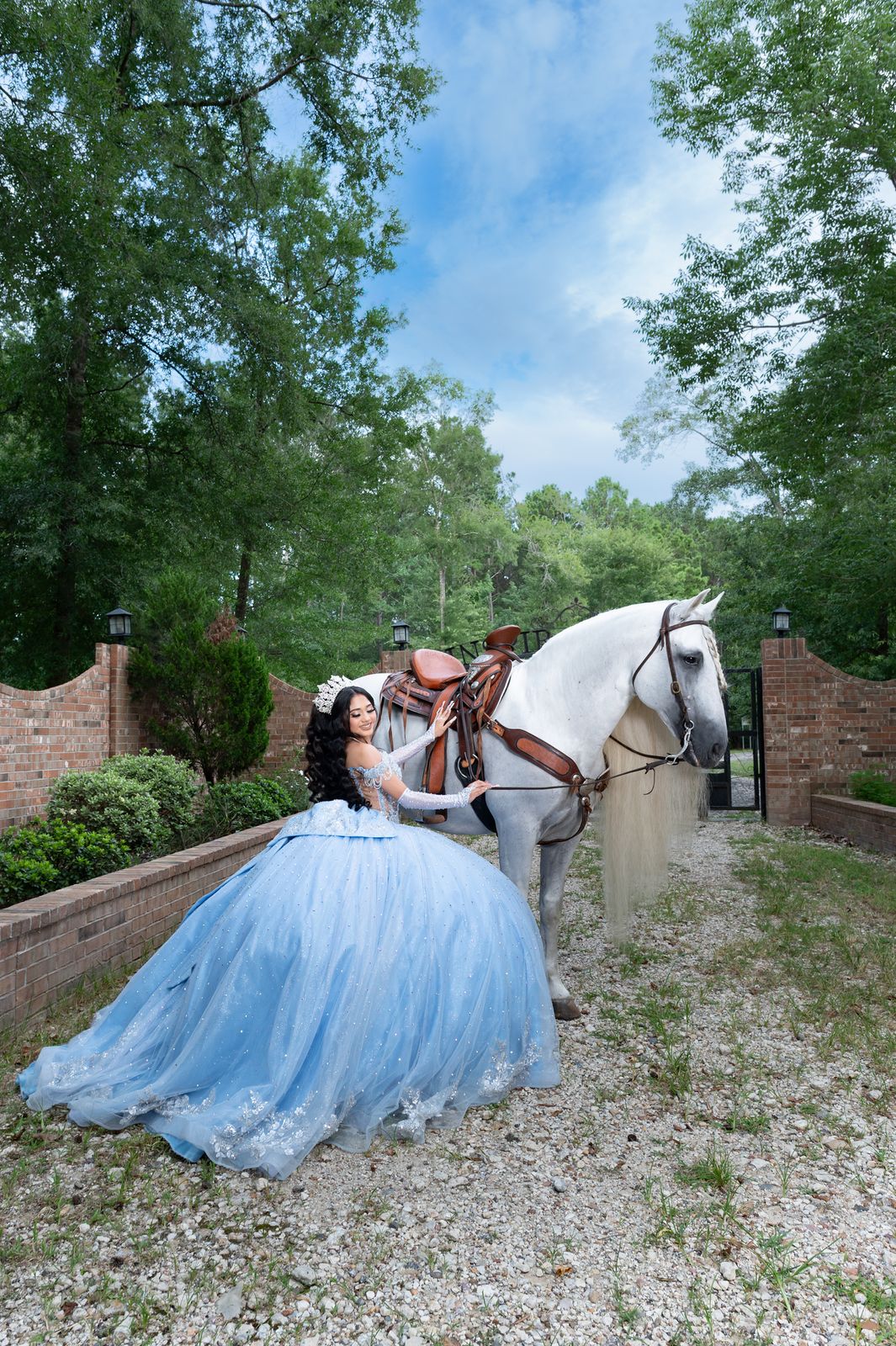Quinceañera seated on the gravel drive with a saddled white horse behind her