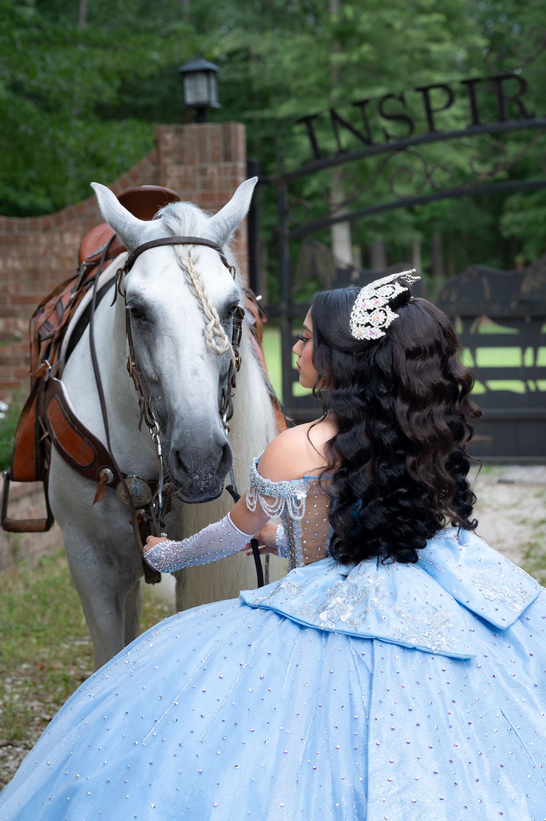 Quinceañera seen from behind reaching up to a white horse at the ranch gate