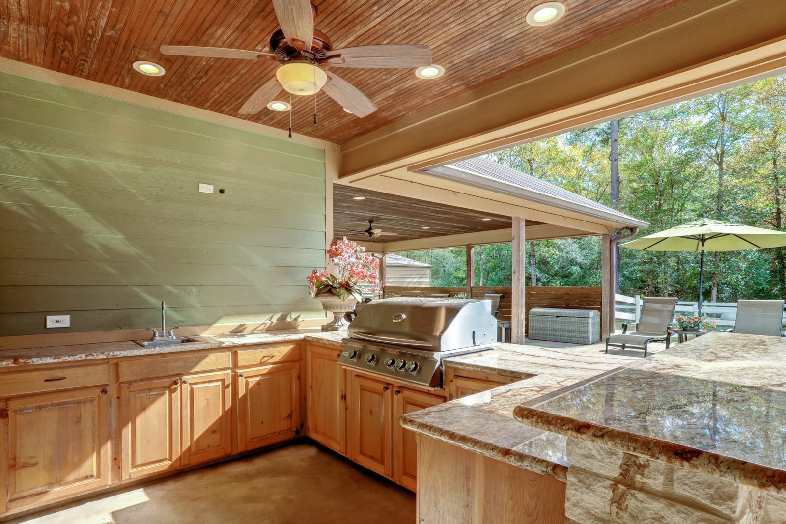Inspira Ranch main house covered patio with built-in grill, wood-beam ceiling, and pool view